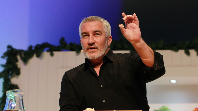 Paul Hollywood speaking on stage with a hand up