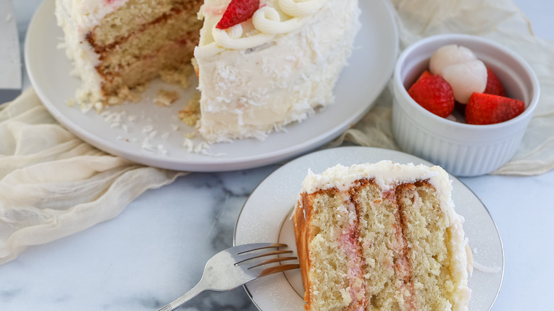 strawberry, coconut, and lychee layer cake on a table with a slice cut out