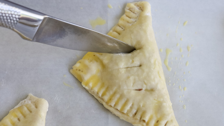 a knife cutting slits into turnover dough