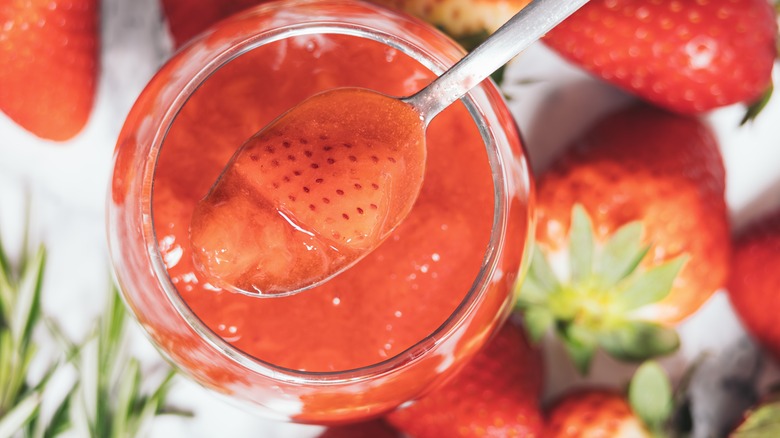 Spoon scooping strawberry puree from a glass jar