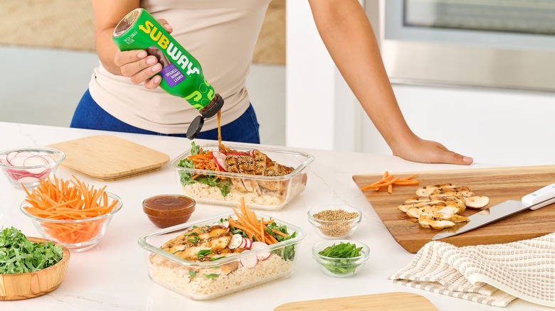 A person pouring bottled Subway teriyaki sauce on a chicken rice bowl