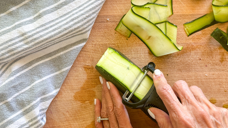 hand peeling zucchini into ribbons