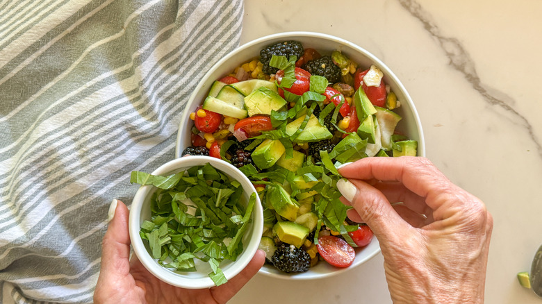 hand adding basil to salad