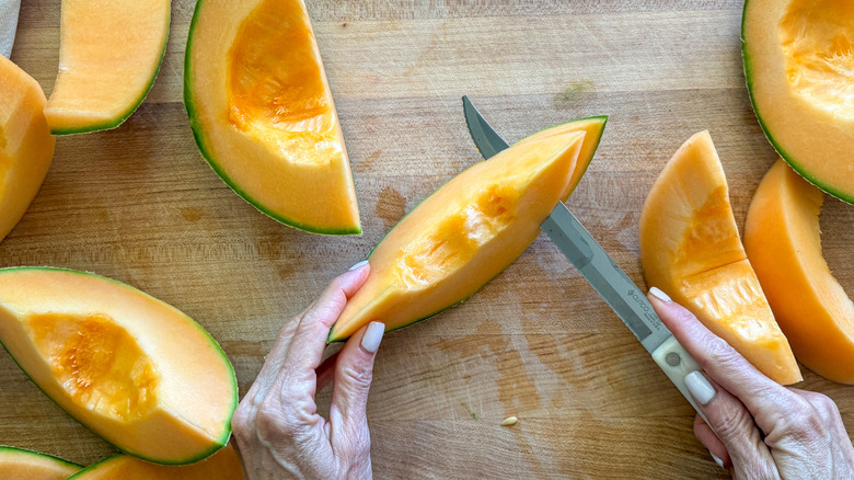 hand slicing off cantaloupe skin