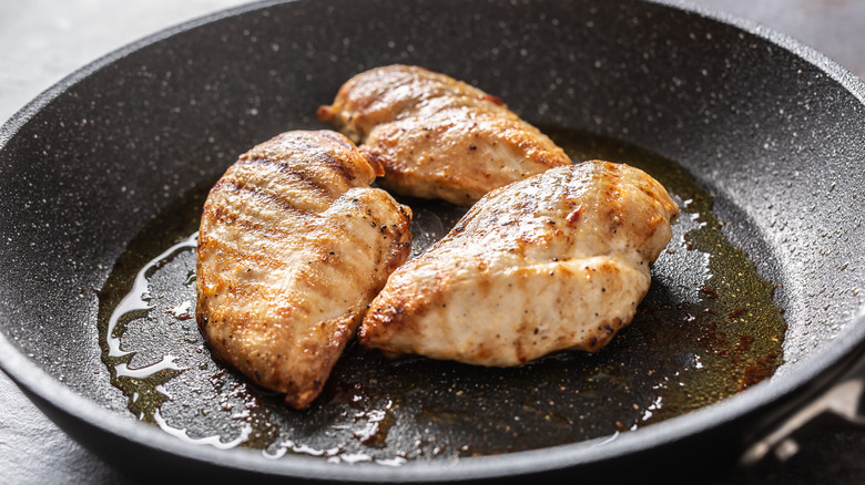 A pan cooking three chicken breasts