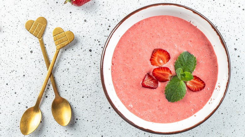 Pink strawberry soup in bowl next to spoons