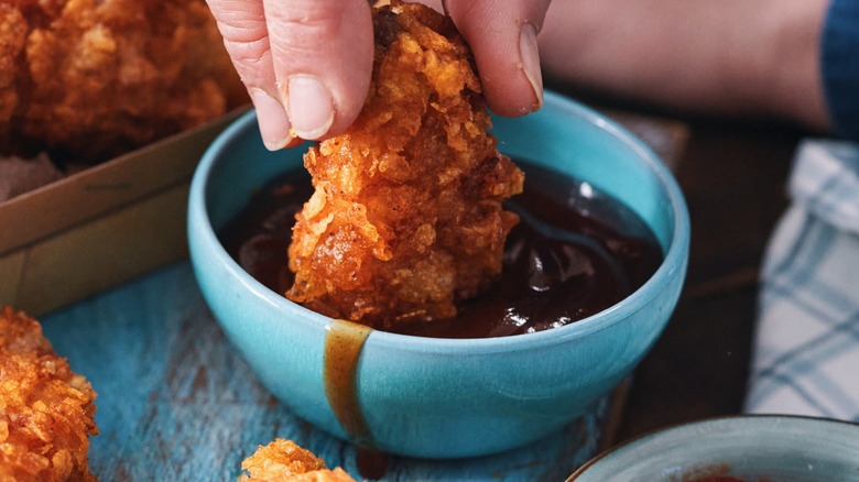 Fingers dunking fried chicken into a sauce