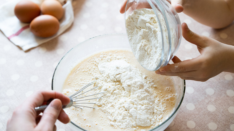 hands adding flour into batter