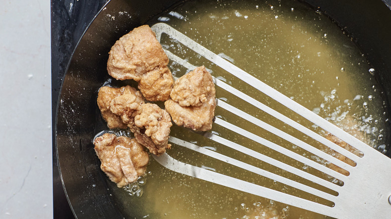 scooping chicken from oil with spatula