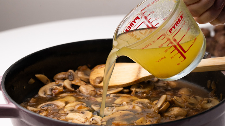 Stock being poured into pan with mushrooms