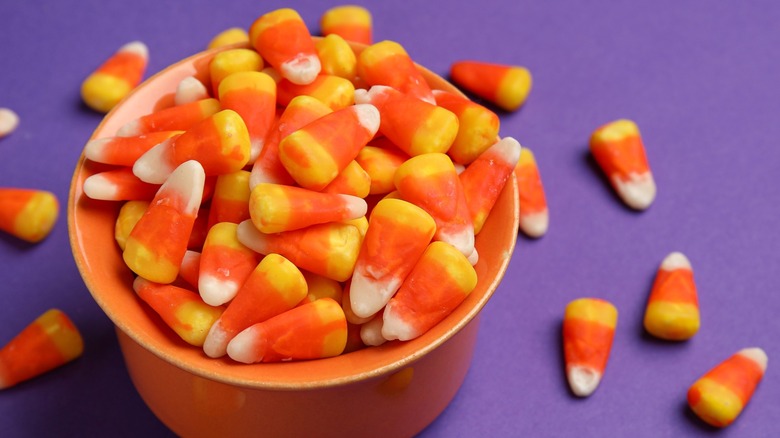 A spilling bowl of candy corn on a purple surface