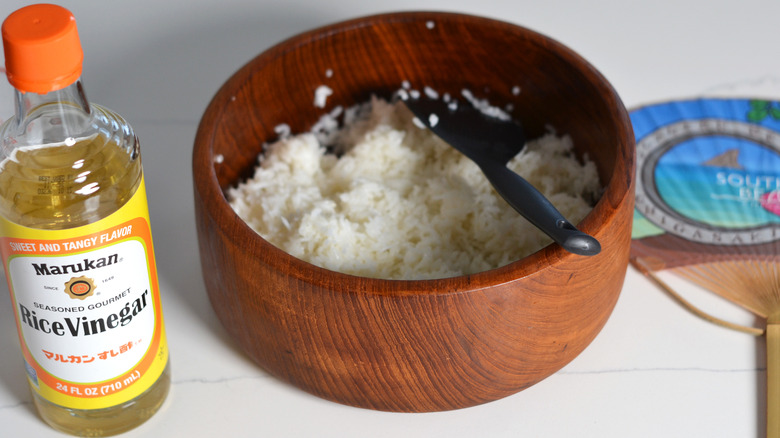 Wooden bowl of rice, bottle of rice vinegar, and a fan