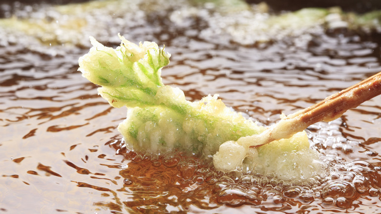 tempura battered green extracted from hot oil with chopsticks