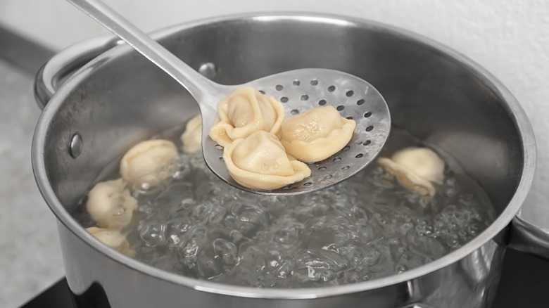 Metal strainer holding pierogi over water