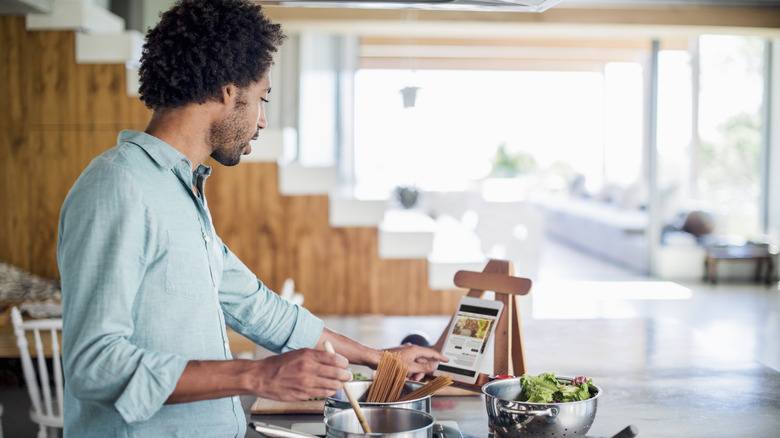 Person cooking in kitchen and swiping tablet while reading a recipe