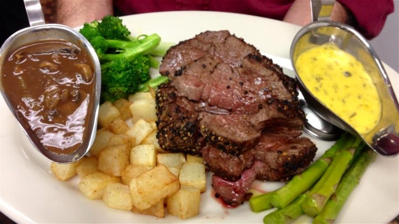 Plate of steak with greens, potatoes, mushroom gravy, and bearnaise sauce