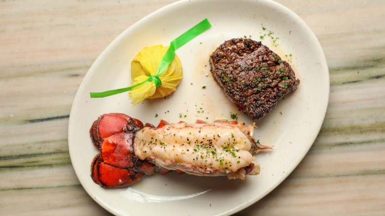 Small filet and lobster tail with bag of salt on white plate