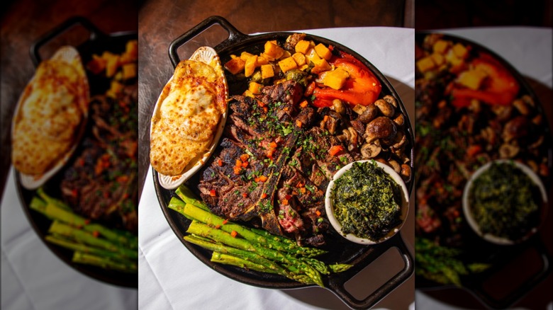 STeak with veggies, creamed spinach, and potatoes au gratin in skillet on white tablecloth