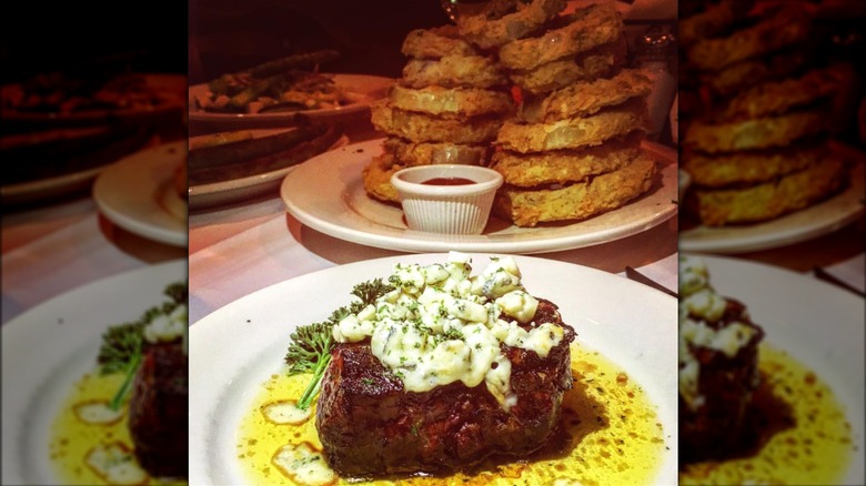 Steak covered in bleu cheese crumbles with huge pile of onion rings in background