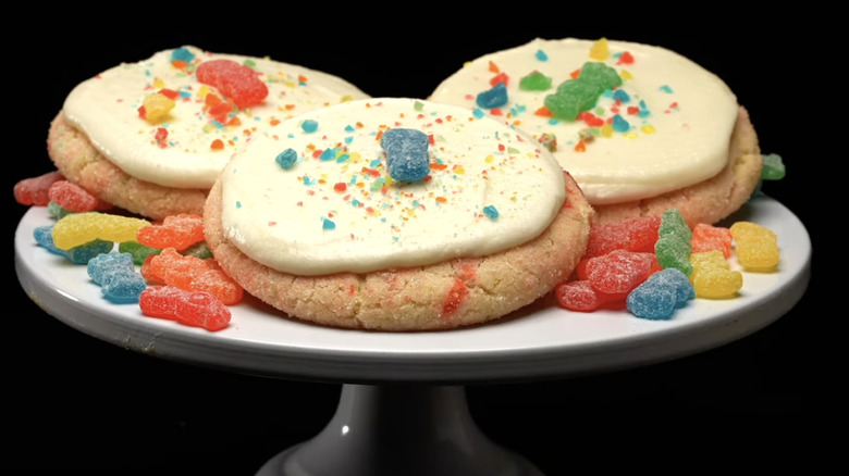 3 sugar cookies with rainbow topping and a sour patch kid on top of a white platter