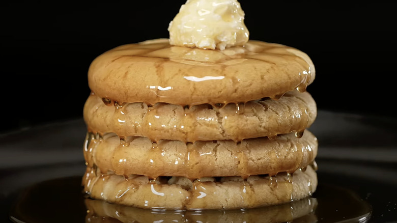 4 yellow waffle cookies stacked on top of each other with a maple syrup glaze and dollop of buttercream on top