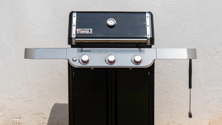 An unplugged Weber Genesis grill standing against a wall.