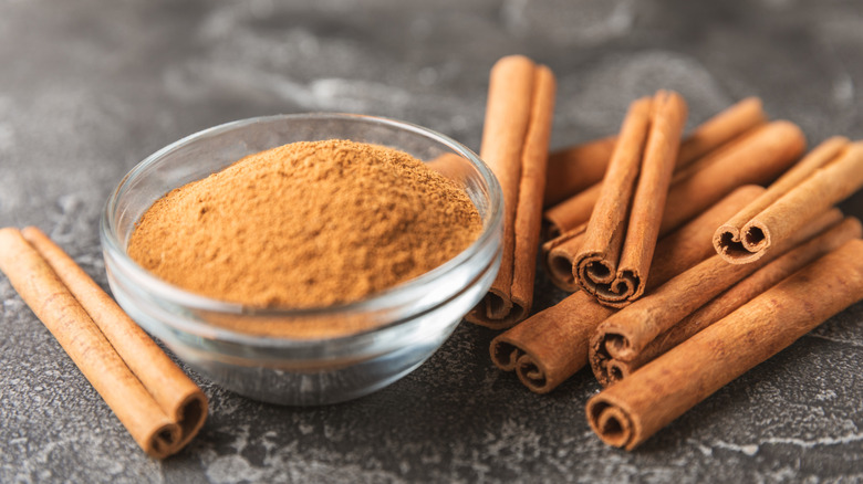 Small dish of cinnamon powder on a table with cinnamon sticks