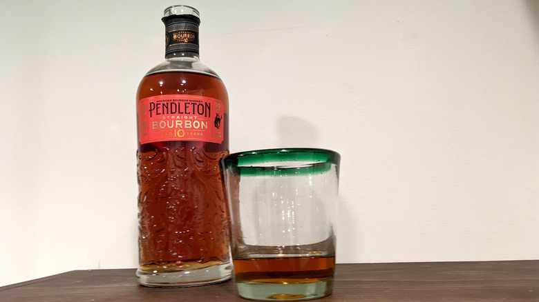 Pendleton 1910 10-Year Straight bourbon bottle and glass on wooden table in front of white wall