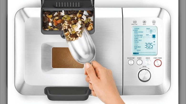 Person scooping fruit and nuts into a tray of the breville bread maker