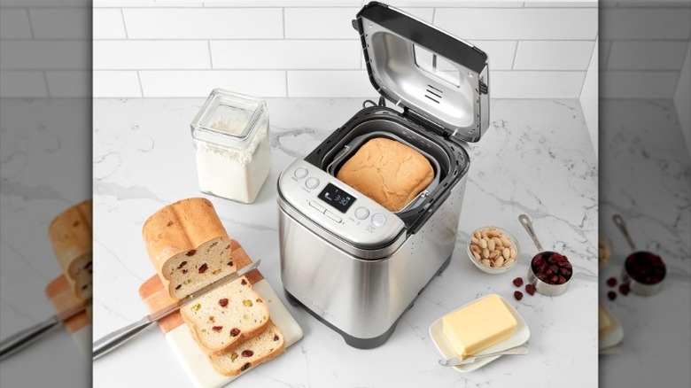 silver Cuisinart bread maker on a counter next to fresh cranberry bread and butter