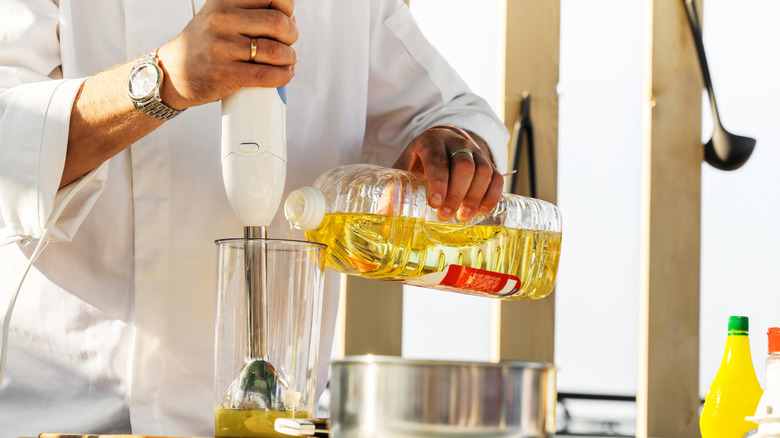 Chef pouring oil to emulsify with immersion blender