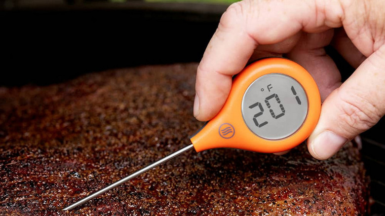 Person holding ThermoPop instant-read thermometer to check grilled meat