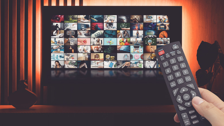 Person holding remote control in front of a TV screen with multiple show icons