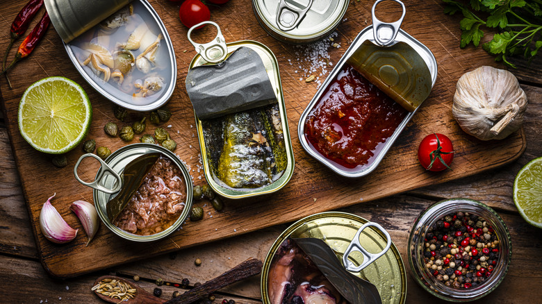 Several open cans of tinned fish on a table with other ingredients