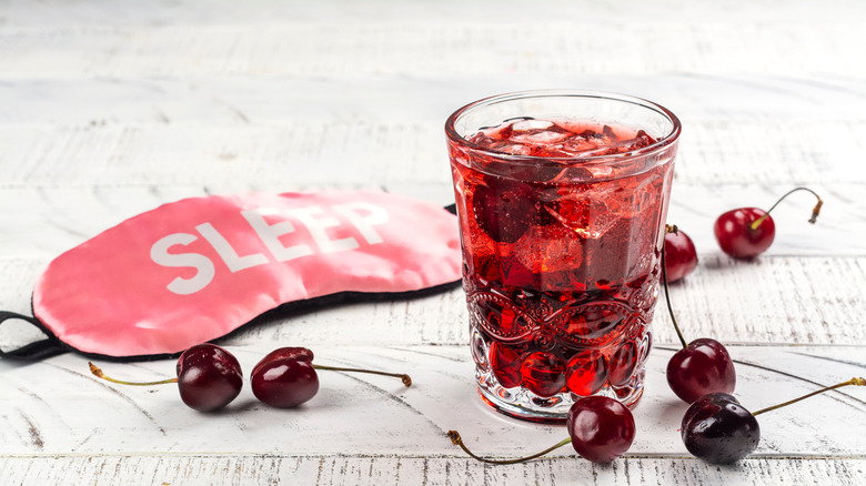 Tart cherry mocktail in a glass surrounded by cherries and a sleep mask