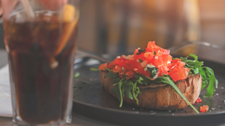 Bruschetta on a black plate next to a soda