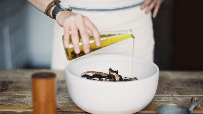 Cook adding olive oil to bowl of mushrooms