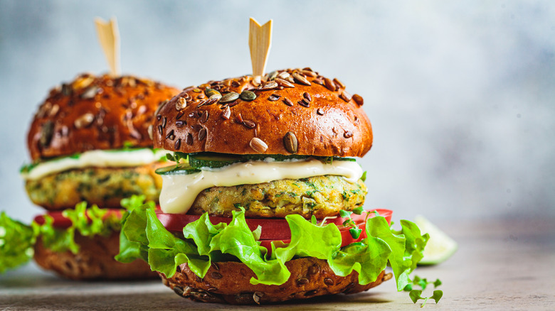 Two homemade falafel veggie burgers with seeded buns, lettuce, and tomato slices