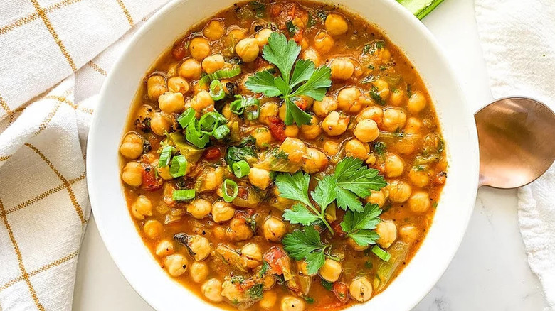 Spiced chana masala in white bowl with beige and white fabric napkin and copper spoon