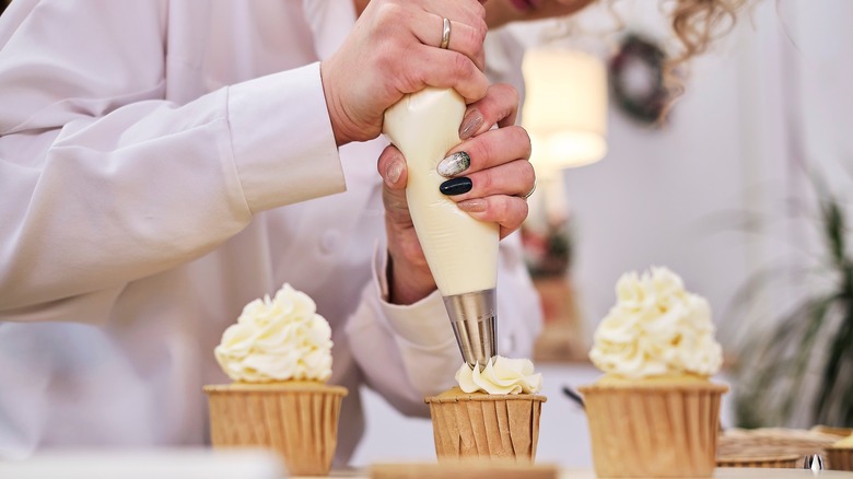 Person piping icing on cupcake