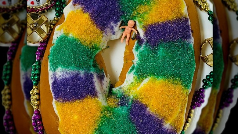 plastic baby inside the ring of a mardi gras colored king cake