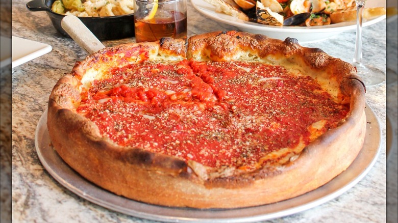 Deep dish pizza on a marble table with glasses