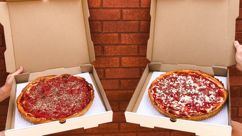 Two pizzas from Two Cities in boxes open in front of a brick wall