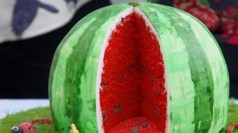 A watermelon shaped cake on top of faux grass with lady bugs.