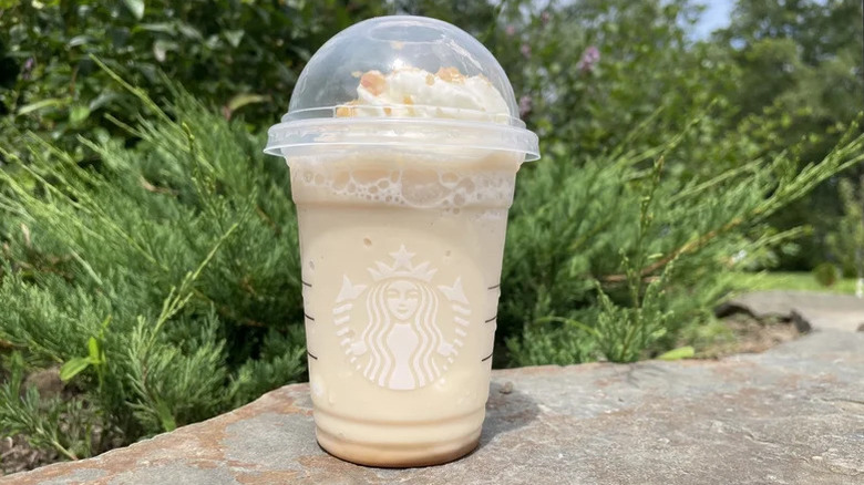 Caramel Ribbon Crunch Crème Frappuccino in a plastic Starbucks cup with greenery and plants in background