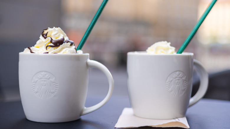 two white Starbucks mugs filled with hot chocolate and topped with whipped cream and chocolate drizzle