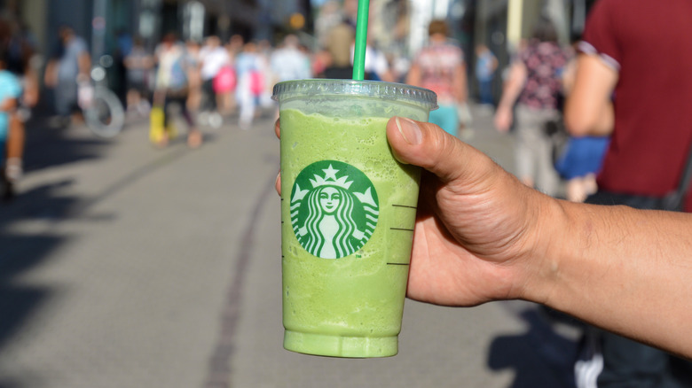 a person on a street holding a Green Tea Matcha Frappuccino in transparent plastic cup