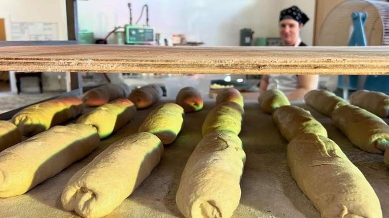 Baguettes proofing on a shelf with worker in the background