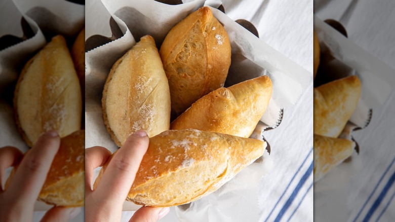 Hand holding a small loaf of french bread with more in wax paper container