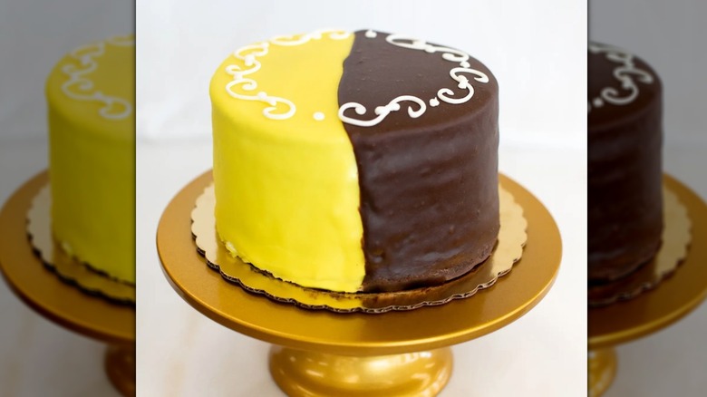 A black and yellow cake on a gold cake stand